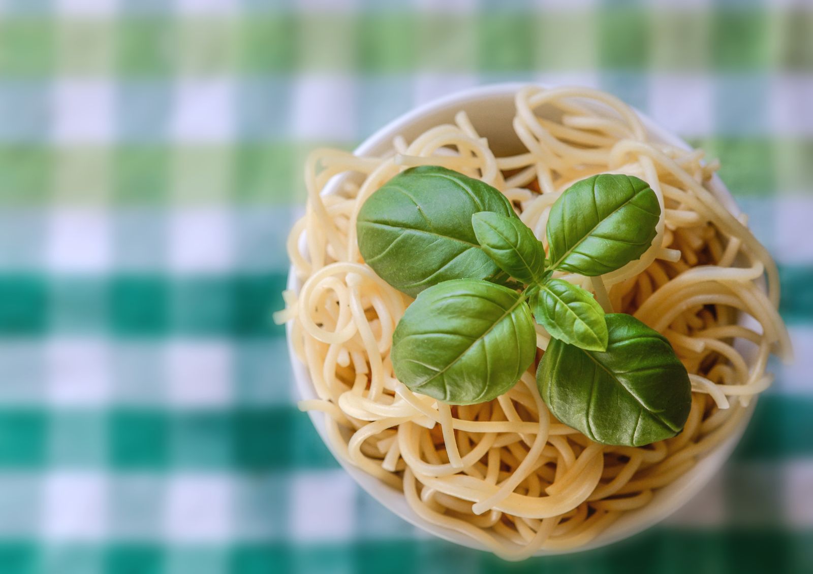 A plate of spaghetti tossed with fresh basil on a checked tablecloth