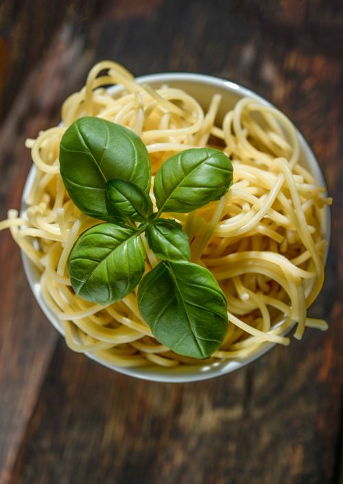 Free Delicious cooked spaghetti with fresh basil leaves arranged on top, perfect for an Italian meal. Stock Photo