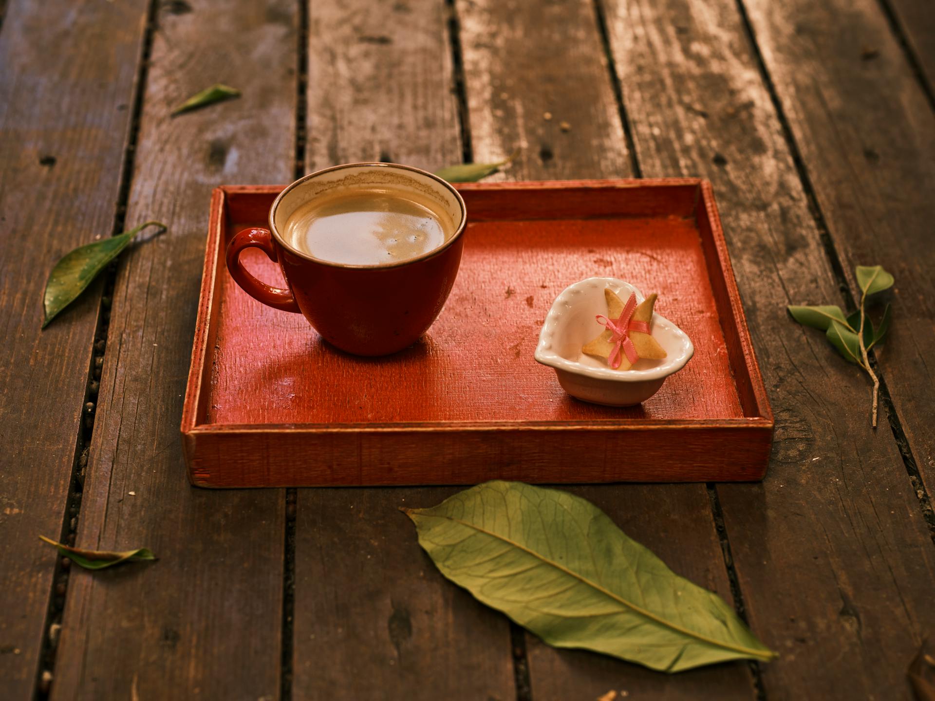 Red coffee cup on a wooden tray with ceramic bowl and leaves, perfect for autumn vibes.