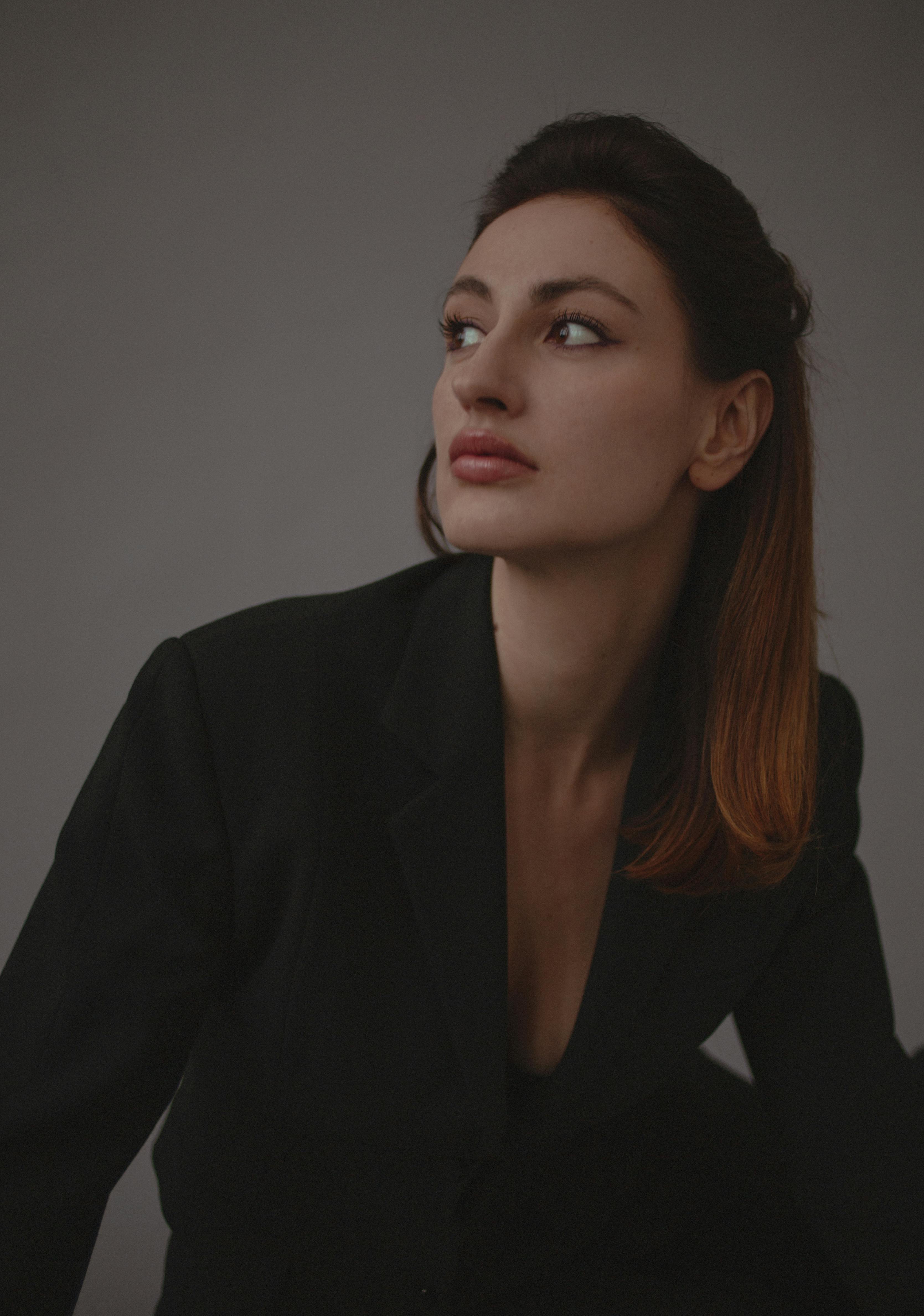 Sophisticated portrait of a woman in a black jacket posing elegantly in a studio setting.
