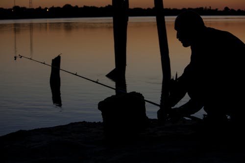 Free Silhouette of Man Fishing Beside Body of Water during Sunset Stock Photo