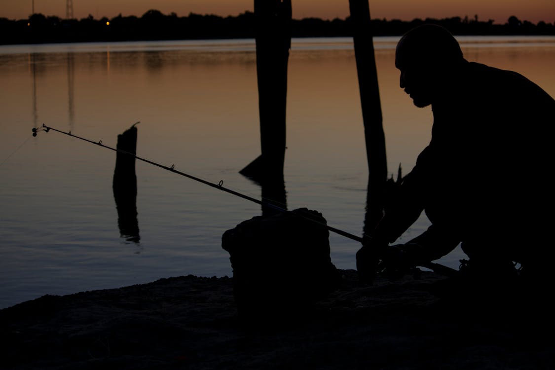 Silhouette of Man Fishing Beside Body of Water during Sunset