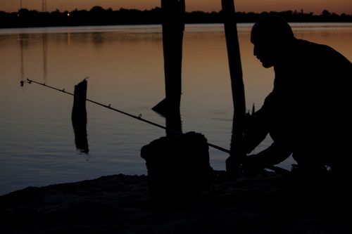 Free A lone fisherman silhouetted against a serene lake at sunset, capturing a peaceful evening scene. Stock Photo