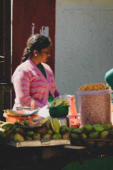A woman vendor selling fruits and snacks at an outdoor market stall.