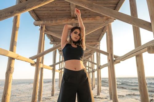 Woman in Black Crop Top and Black Pants Standing Under Brown Wooden Dock