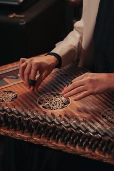 An artistic close-up of hands tuning a traditional kanun string instrument, highlighting intricate details.