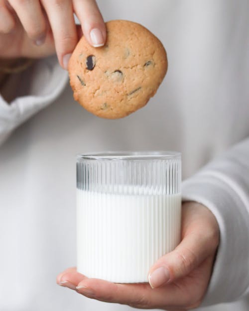 Person Holding a Glass of Milk and Chocolate Chip Cookie 