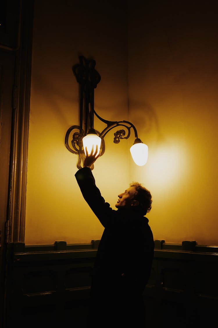 A Man Changing A Light Bulb In A Sconce 