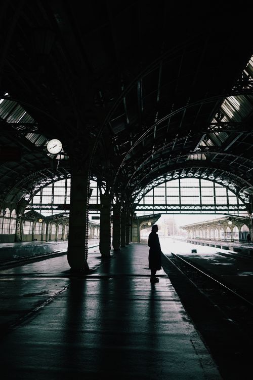 Free Silhouette of a person standing on a historic train station platform, creating a dramatic scene. Stock Photo