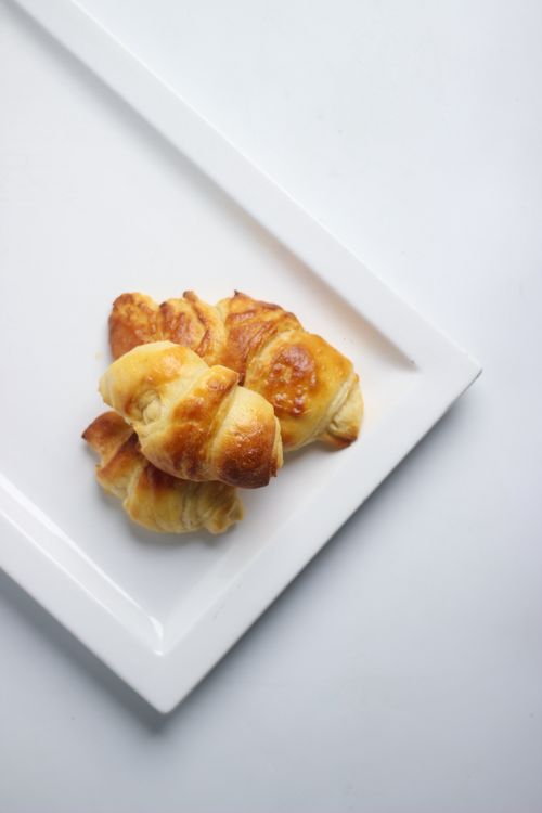 Free Freshly baked croissants arranged on a sleek white ceramic plate, ideal for food photography. Stock Photo