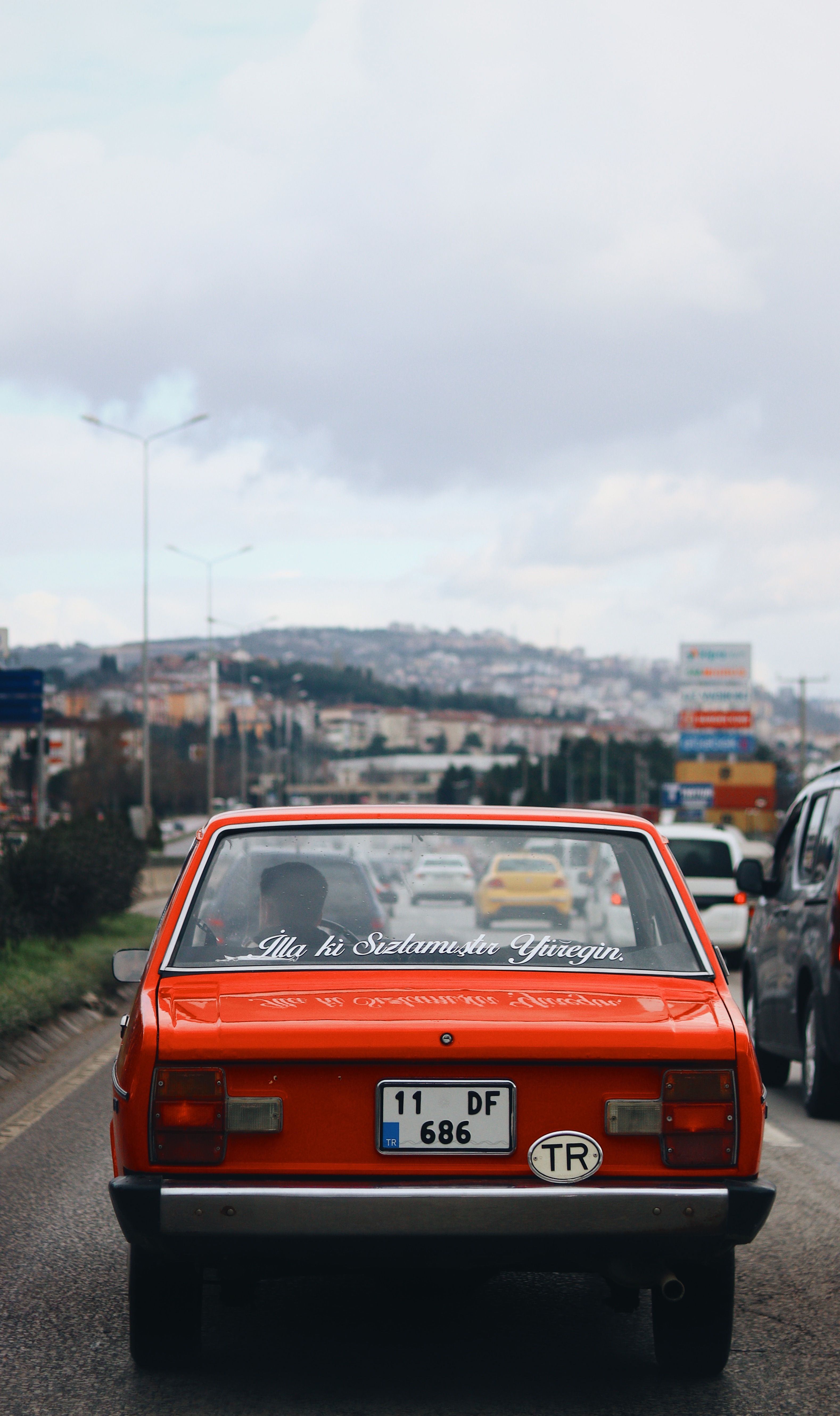A vibrant red vintage car driving on a busy road in İzmit, Kocaeli, Turkey.