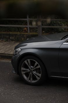 Detailed close-up of a black luxury car's front on a city street, highlighting the wheel and headlight.