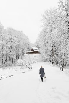 Woman walking on a snowy path with a cozy cabin in the background during winter.