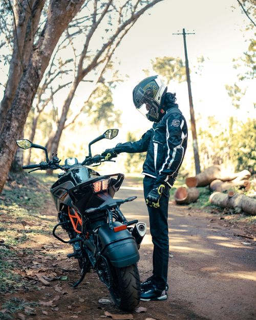 Free Man standing by motorcycle on rural road, wearing full gear and helmet, vibrant autumn setting. Stock Photo
