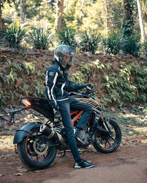 Free A motorcyclist in full gear takes a break on a sunlit forest trail, showcasing adventure and freedom. Stock Photo