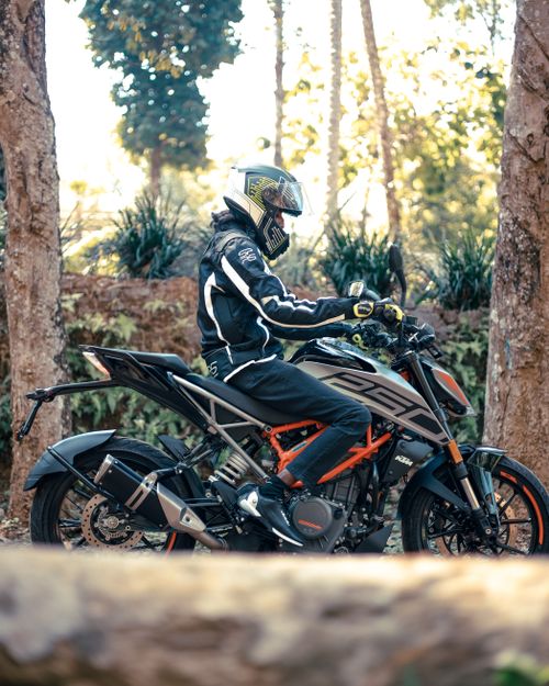 Free A biker on a KTM motorcycle traversing a forested path with sunlight filtering through trees. Stock Photo