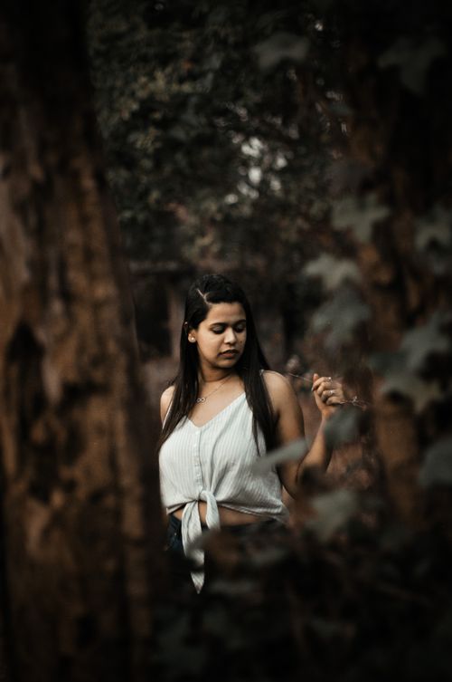 Free A young woman in a white top stands contemplatively in a peaceful forest area. Stock Photo