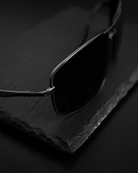 Sleek sunglasses on textured surface in black and white, emphasizing luxury fashion.