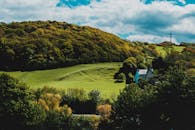 在美丽的山坡乡村，郁郁葱葱的绿色田野和古雅的房子之间，多云的天空下树木充满生机