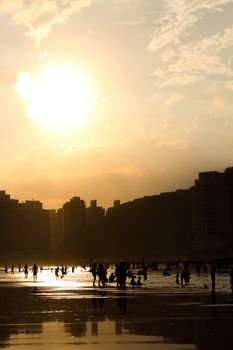 Capture of silhouetted people enjoying a serene sunset on a lively beachfront with a glowing skyline.