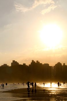 Beachgoers silhouetted against a stunning sunset with city skyline in the background.