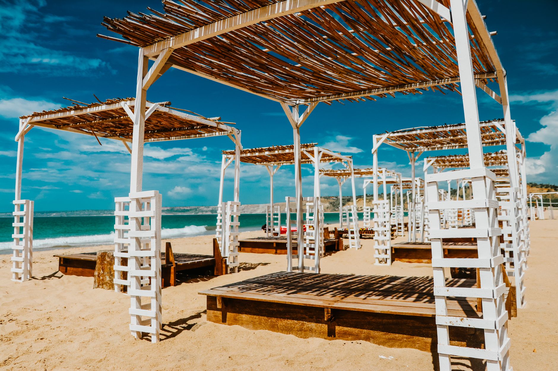 Relaxing beachfront view with wooden loungers and straw pergolas in a tropical resort.