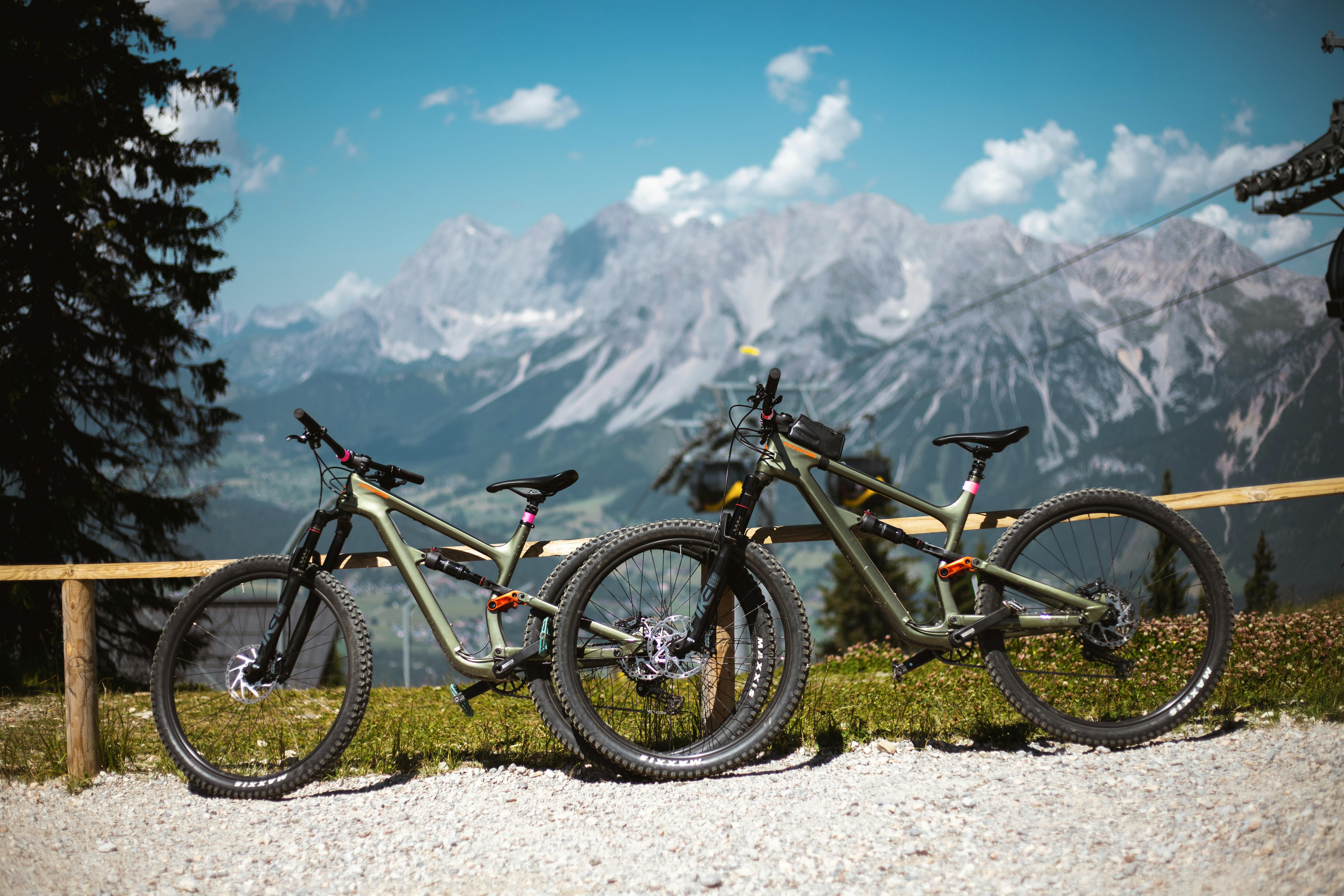 Two mountain bikes resting against a wooden fence with the breathtaking Austrian Alps in the background.