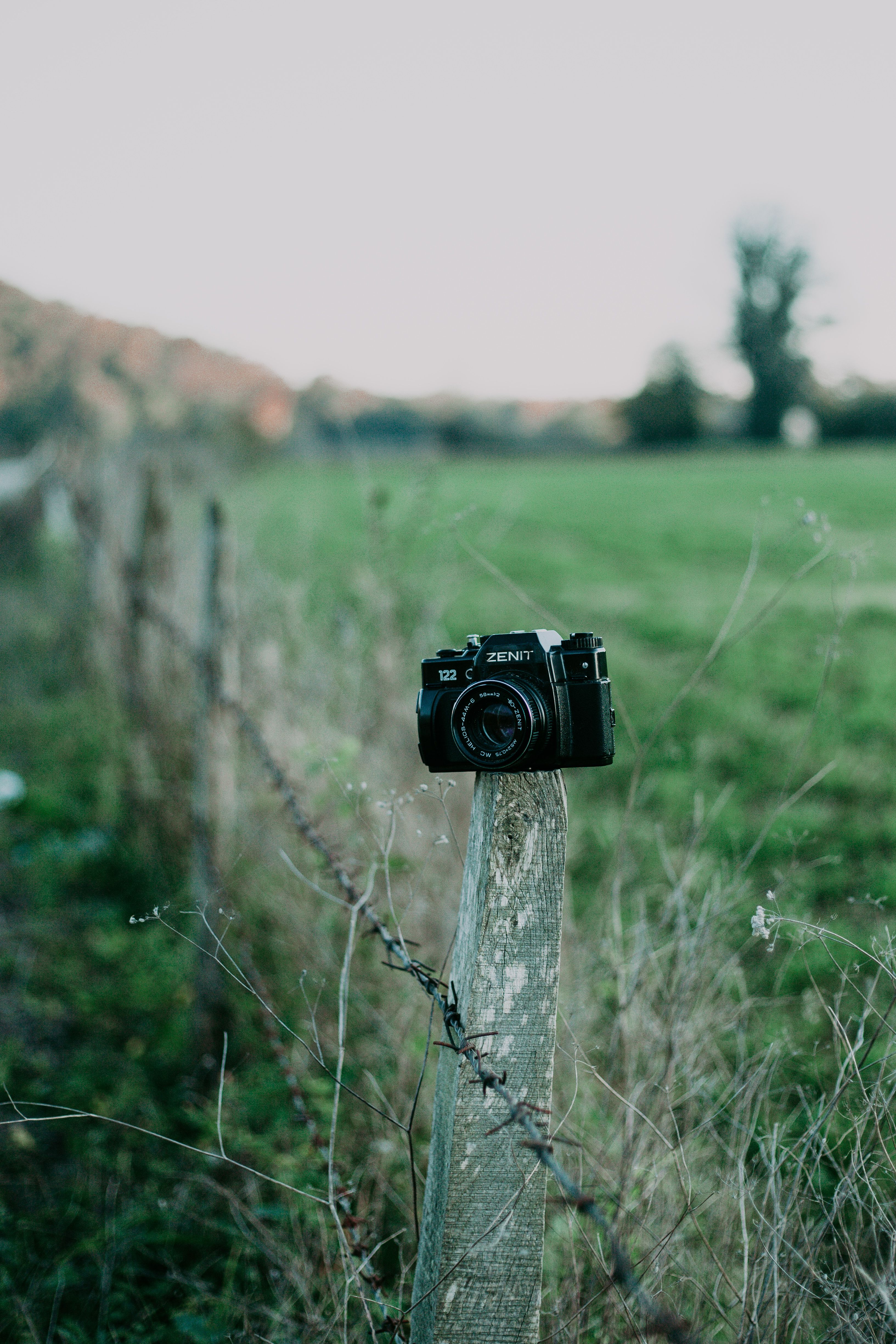 A vintage Zenit camera placed on a wooden post in a rural green field.