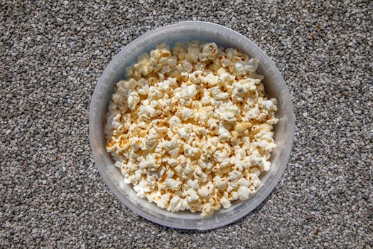 Close-up of buttery popcorn in a clear bowl set on a textured pebble surface.