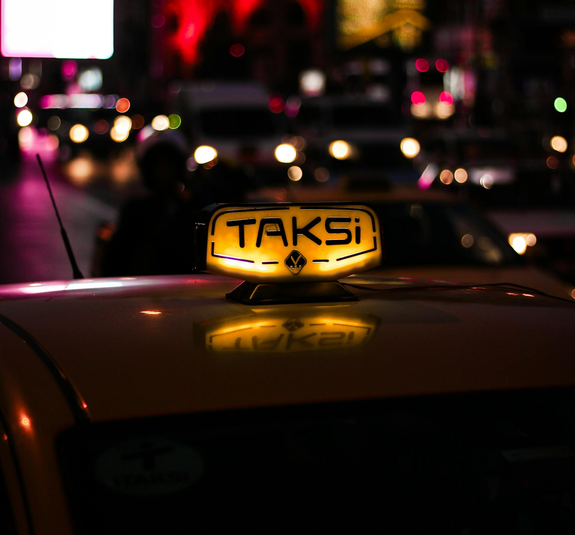 Nighttime scene in Istanbul featuring an illuminated taxi sign against a backdrop of city lights.