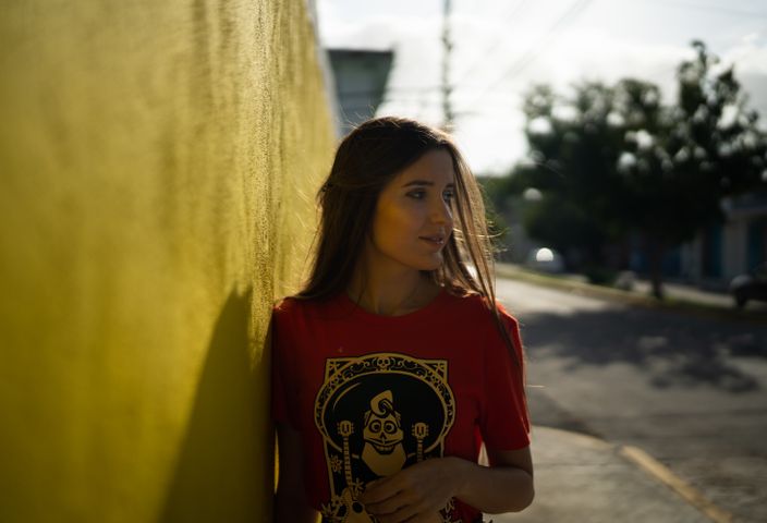 Portrait of a woman in a red shirt leaning against a vibrant yellow wall in Playa del Carmen, Mexico.