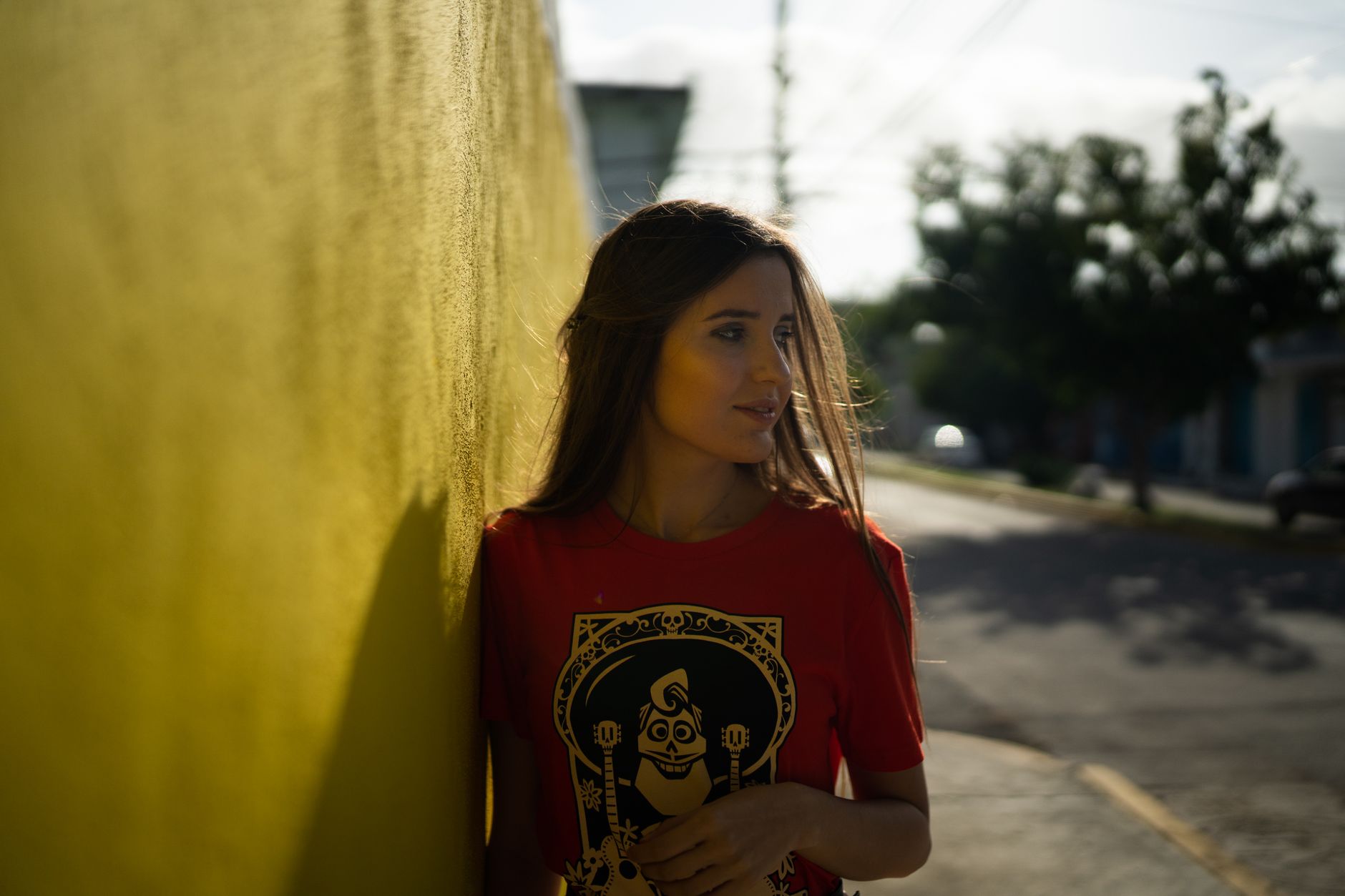 Portrait of a woman in a red shirt leaning against a vibrant yellow wall in Playa del Carmen, Mexico.