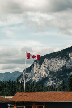 A Canadian flag waves on a flagpole against a mountainous landscape in Alberta. Ideal for nature and travel content.