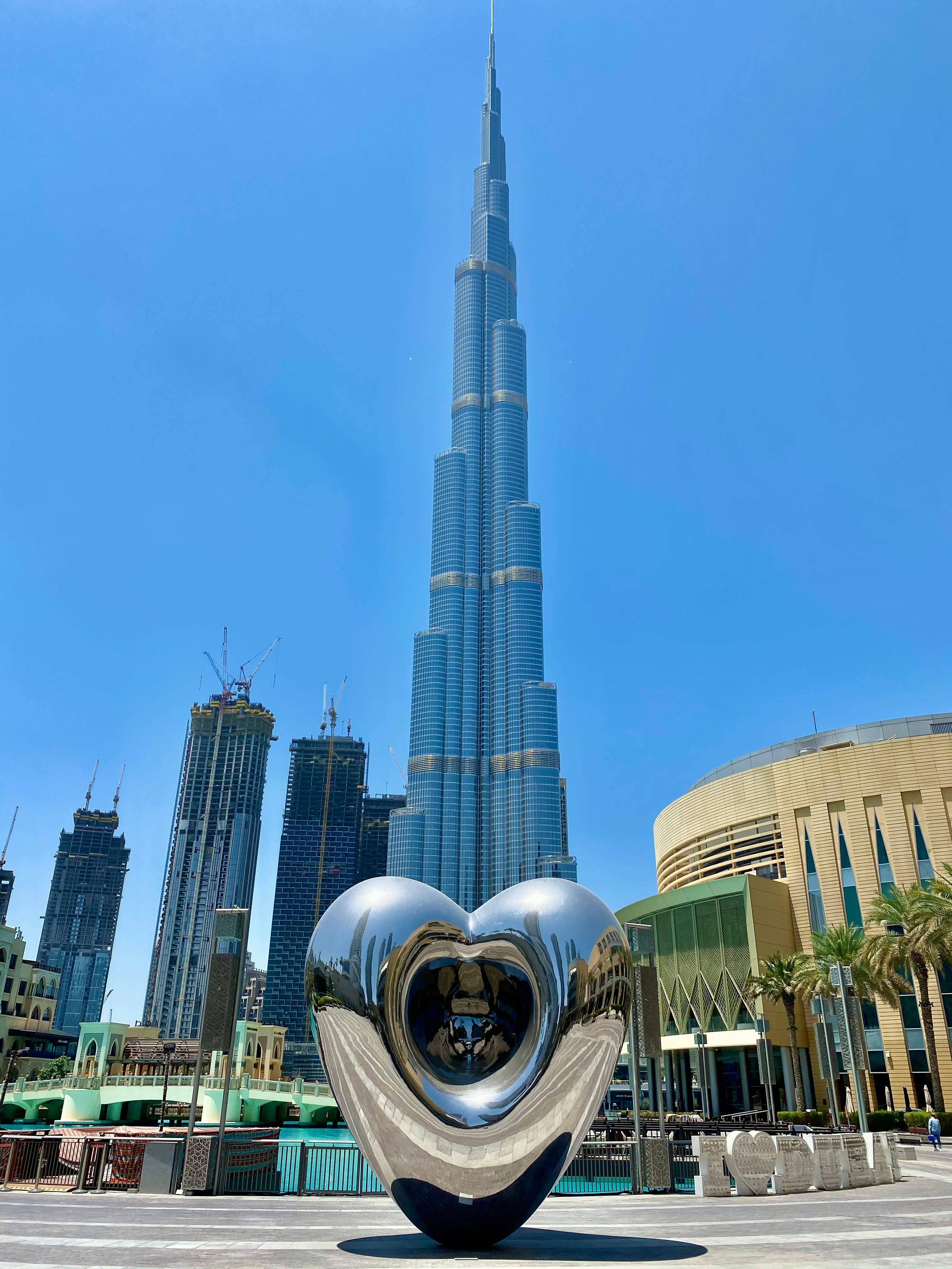 A striking view of Burj Khalifa and a heart sculpture under a clear blue sky in Dubai.