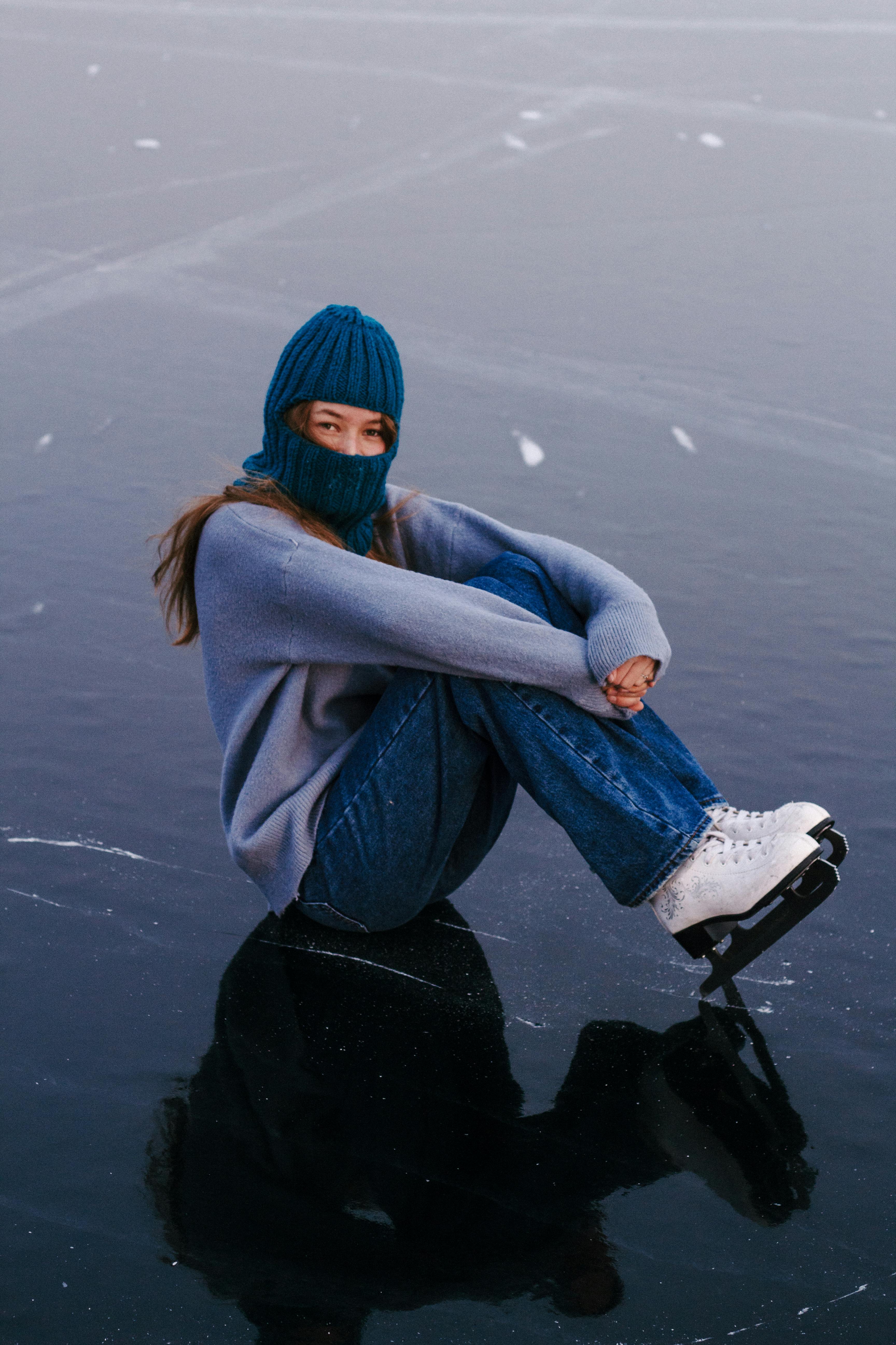 A woman dressed warmly sits on a frozen lake wearing ice skates, exuding winter charm.