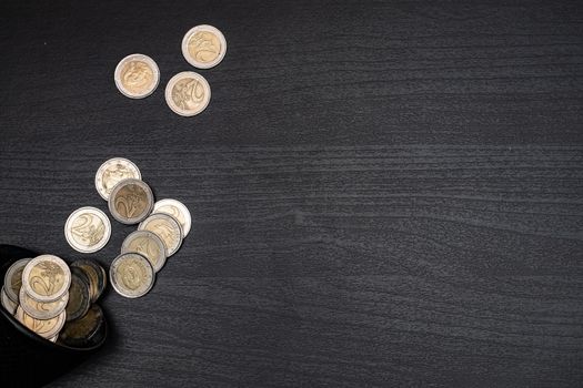 A collection of euro coins scattered on a dark textured surface, with space for text.