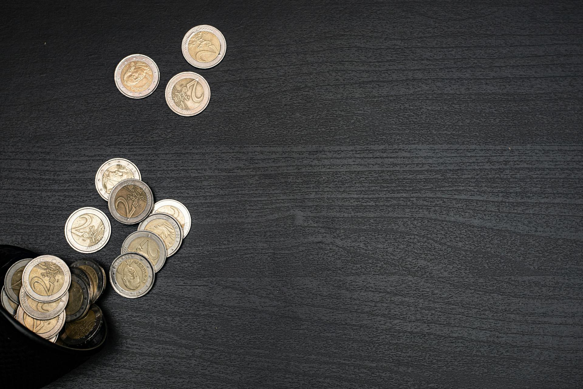 A collection of euro coins scattered on a dark textured surface, with space for text.