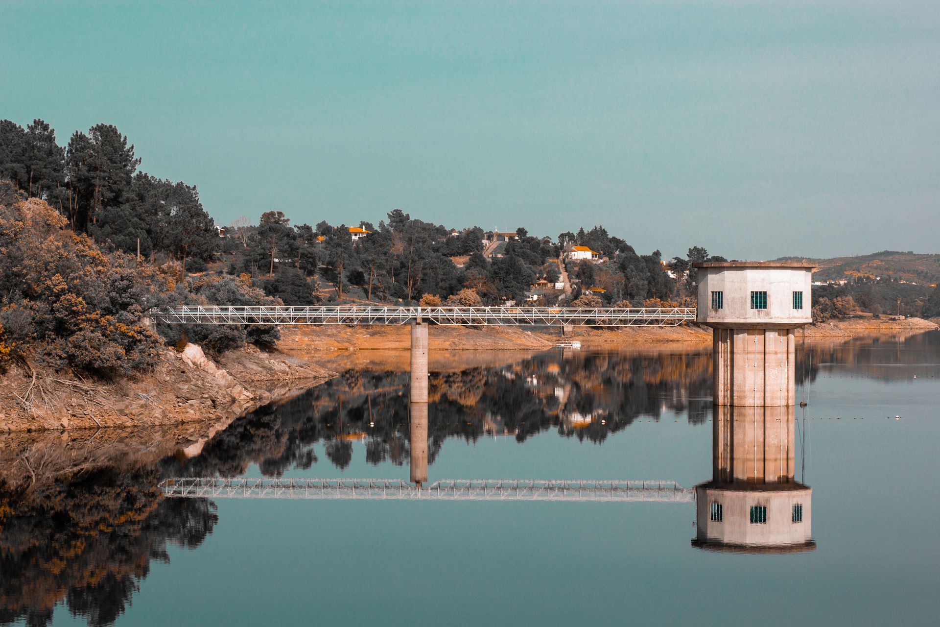 A peaceful lakeside scene showcasing a reflective intake tower and bridge against a forested backdrop.