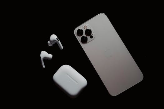 Close-up of smartphone and wireless earbuds on a dark surface, showcasing modern tech gadgets.