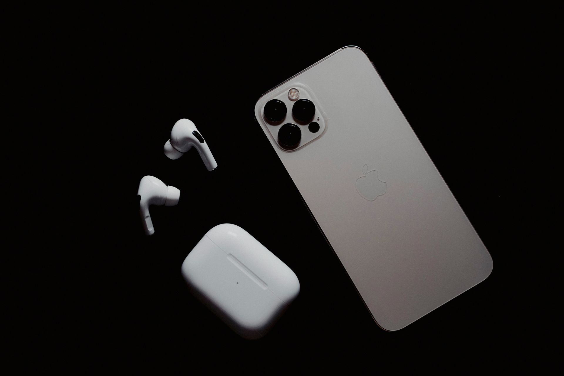 Close-up of smartphone and wireless earbuds on a dark surface, showcasing modern tech gadgets.