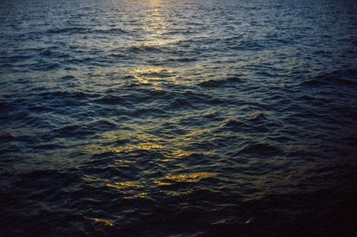 Free Serene ocean waves reflecting the golden hues of a sunset, creating a peaceful seascape. Stock Photo