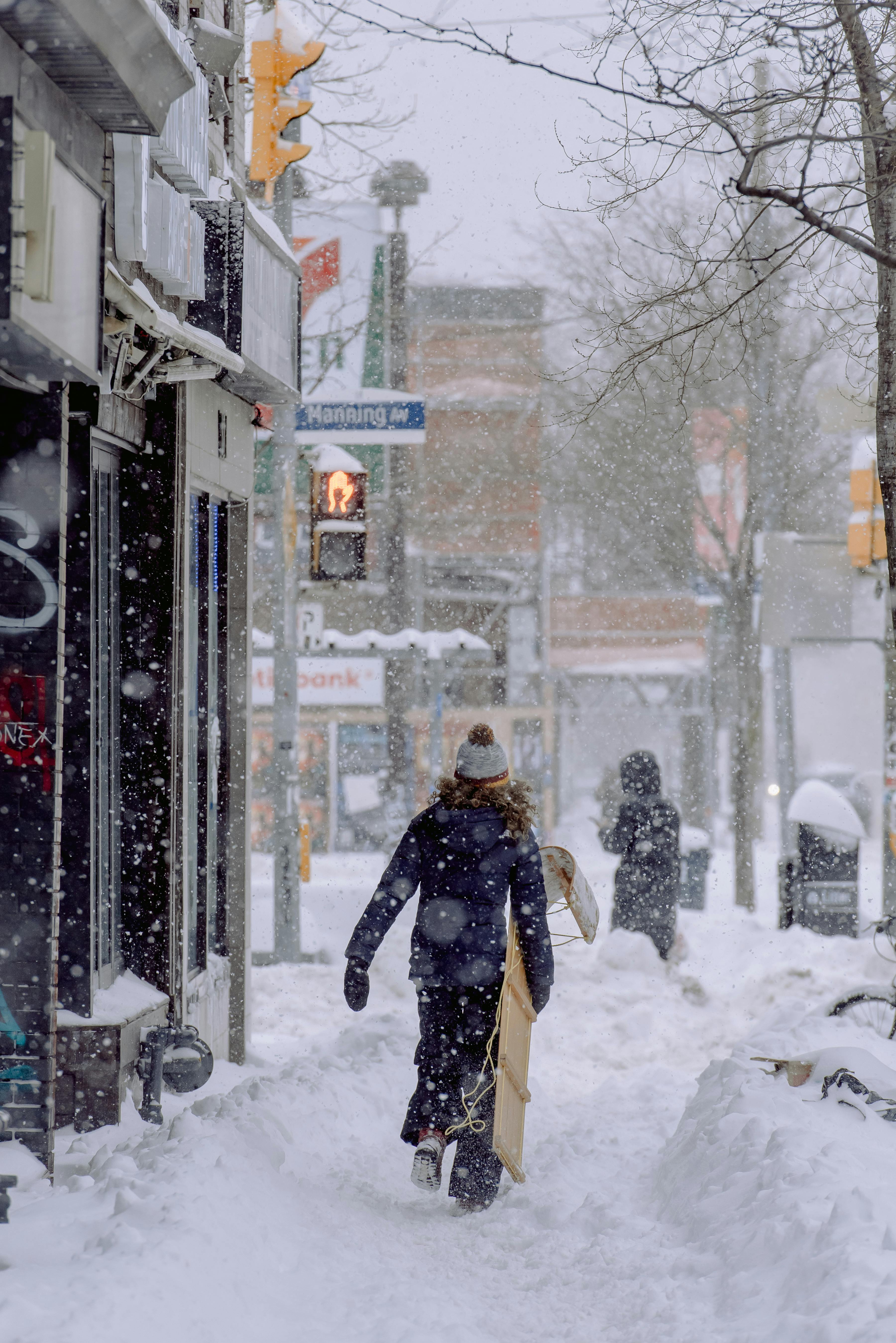 A person walks through a snowy urban street as snowflakes fall in a winter wonderland.