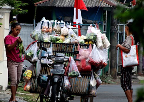 A street vendor on a motorbike sells fresh vegetables and fruit in a vibrant outdoor market.