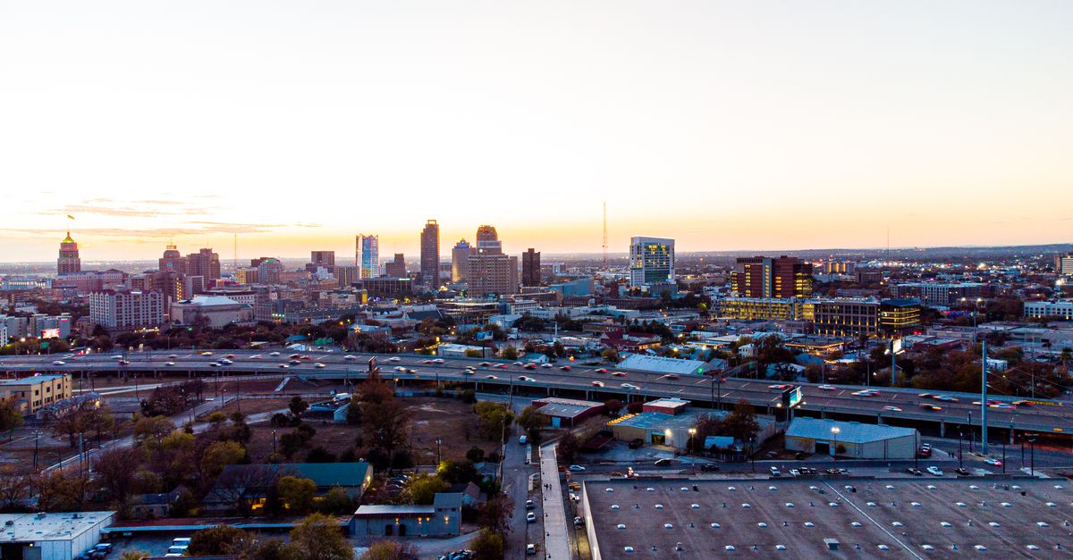 Aerial view of San Antonio skyline at sunset with downtown high-rise buildings glowing under an orange sky