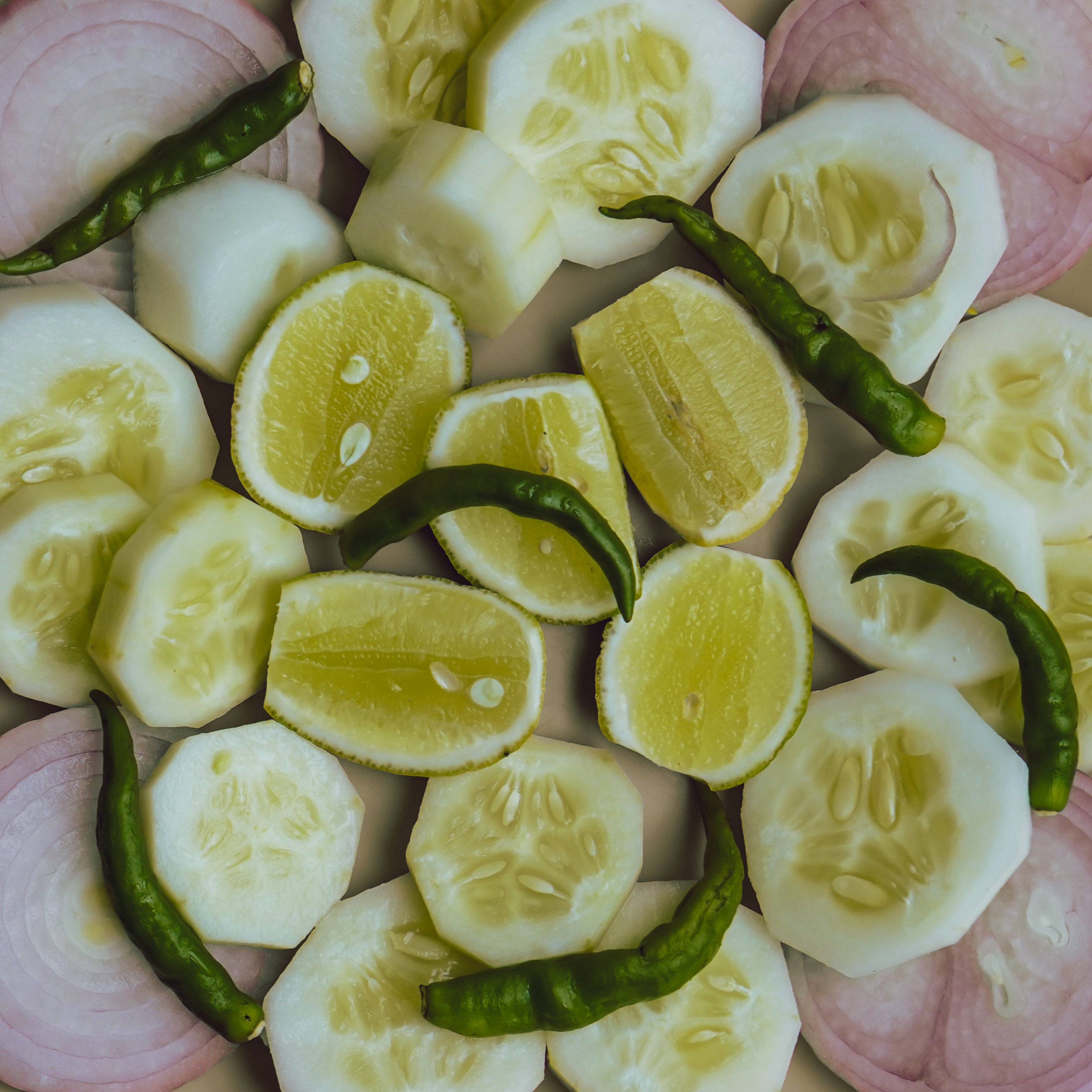 Overhead arrangement of sliced cucumbers, onions, green chilies, and lime.