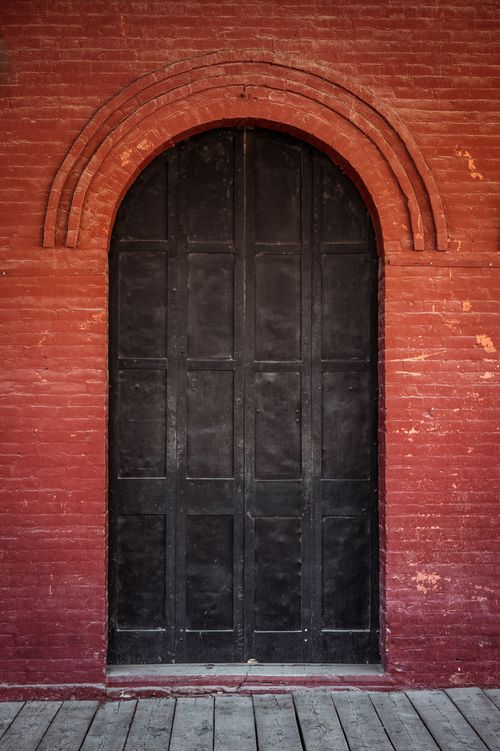 Free A sturdy arched wooden door set in a red brick wall, exuding vintage charm. Stock Photo