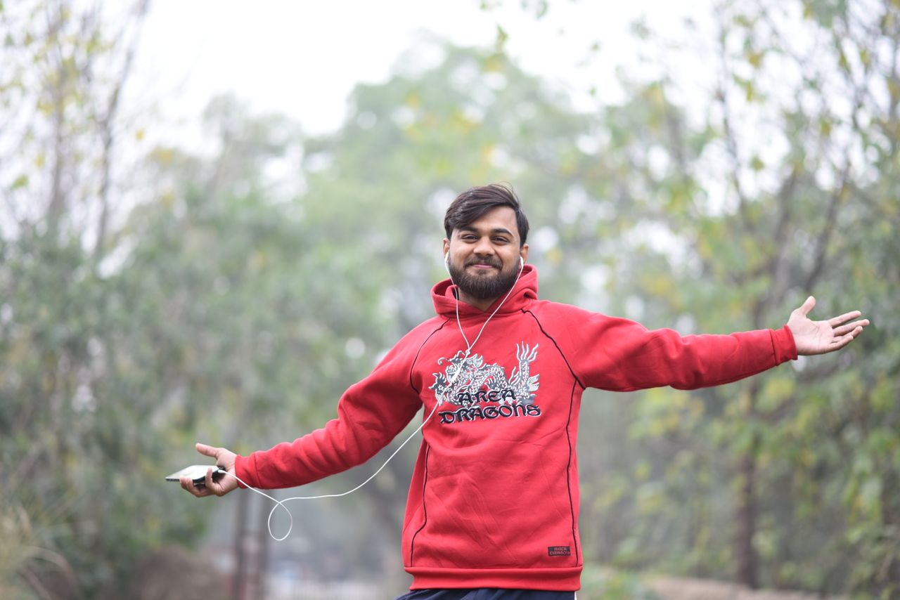 a smiling man in a red hoodie enjoying a leisurely walk outdoors exudi