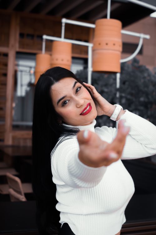 Free Elegant woman in a white turtleneck posing with a smile and reaching hand forward indoors. Stock Photo