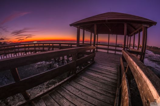A stunning sunset view from a wooden pier overlooking the tranquil sea.
