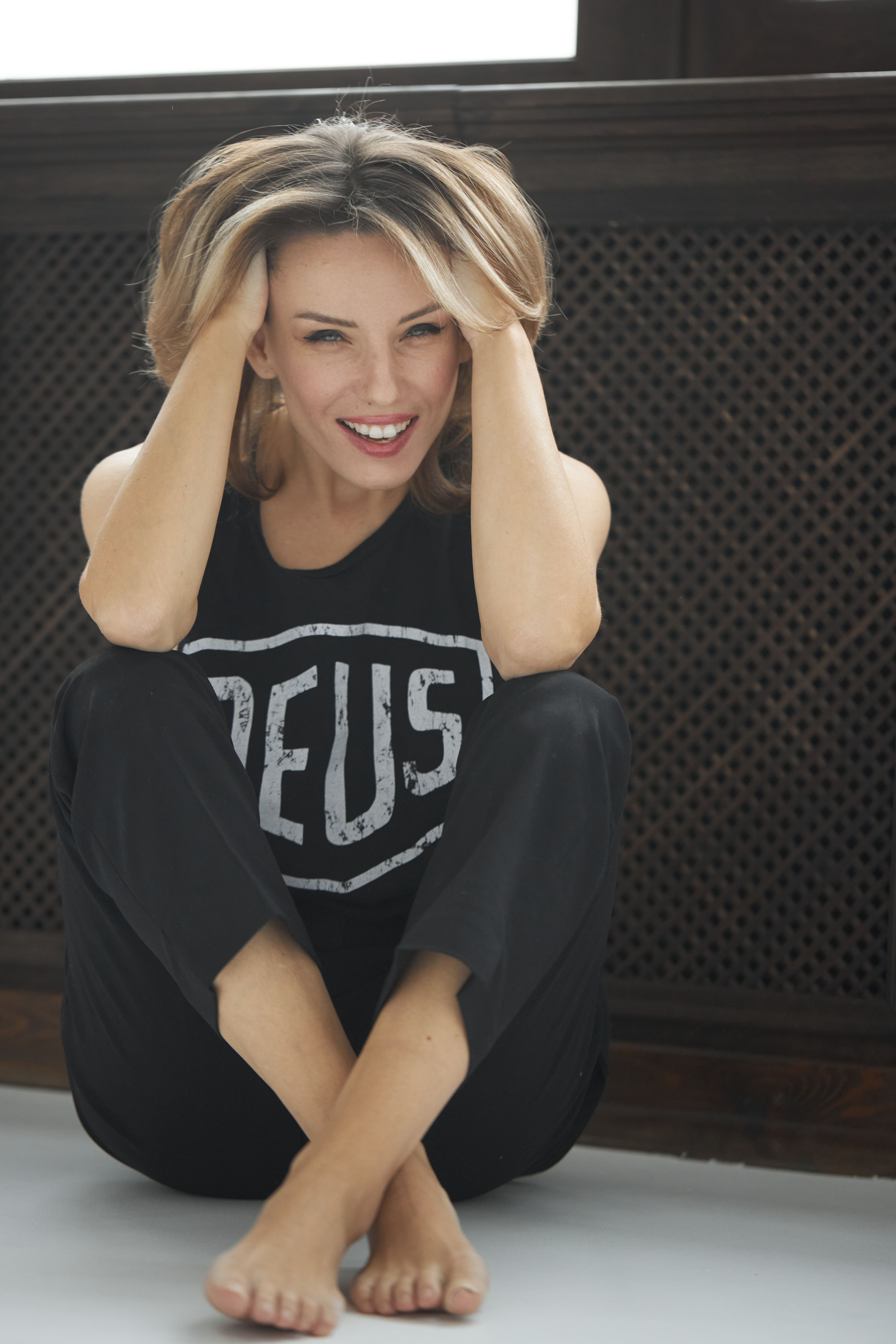 Cheerful woman with blond hair in casual clothing sitting inside, smiling joyfully.